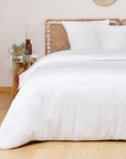 White comforter on a bed with a wooden headboard and side table in a room.